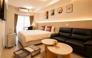 A hotel room with a bed, a black leather sofa, two round tables, a wall-mounted TV, and an air conditioning unit. - Hotel Arashi Nambaminami No003 (Osaka)