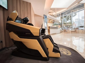 Ein Massagesessel in einer modernen Hotelhalle mit Glaswand und einer Rezeption.