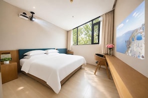 Ein modernes Schlafzimmer mit einem großen Bett, einem Schreibtisch, einem Stuhl, einem Nachttisch, einer Wandlampe und einem Fenster mit Blick auf Grünflächen.