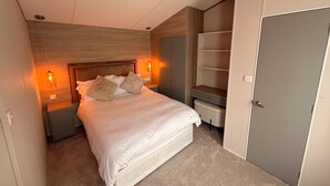 A bedroom with a bed, bedside tables, a wardrobe, and a door. - Cabin Sleeps 6 With Lake Access Parking (Northampton)