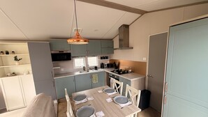 A compact kitchen with a dining area, featuring a wooden table, chairs, and a hanging light fixture. - Cabin Sleeps 6 With Lake Access Parking (Northampton)