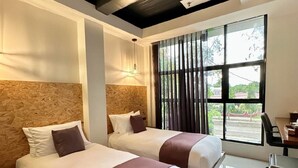 A hotel room with two beds, a desk, and a large window with curtains. - Koze Suites (Dumaguete)
