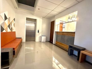 A modern lobby with a reception desk, a bench, an elevator, and a wall-mounted artwork. - Koze Suites (Dumaguete)