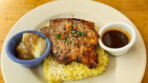 A plate with yellow rice, a piece of meat, a small bowl of sauce, and a small bowl of gravy. - Koze Suites (Dumaguete)