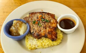 A plate with yellow rice, a piece of meat, a small bowl of sauce, and a small bowl of gravy. - Koze Suites (Dumaguete)