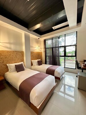 A hotel room with two beds, a desk, and a large window with curtains. - Koze Suites (Dumaguete)