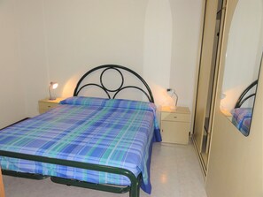 Ein Einzelbett mit Metallgestell, eine blaue und grüne Karo-Bettdecke, zwei Nachttische mit Lampen und ein großer Spiegel an der Wand.