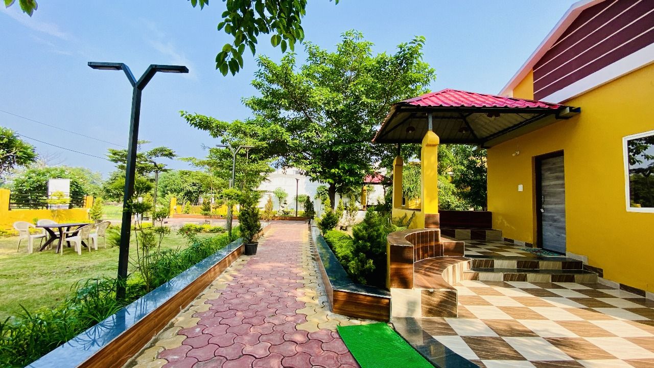 A pathway leading to a yellow building with a red roof, surrounded by greenery and a clear sky.