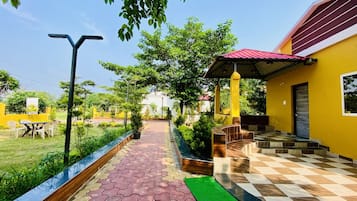 A pathway leading to a yellow building with a red roof, surrounded by greenery and a clear sky.