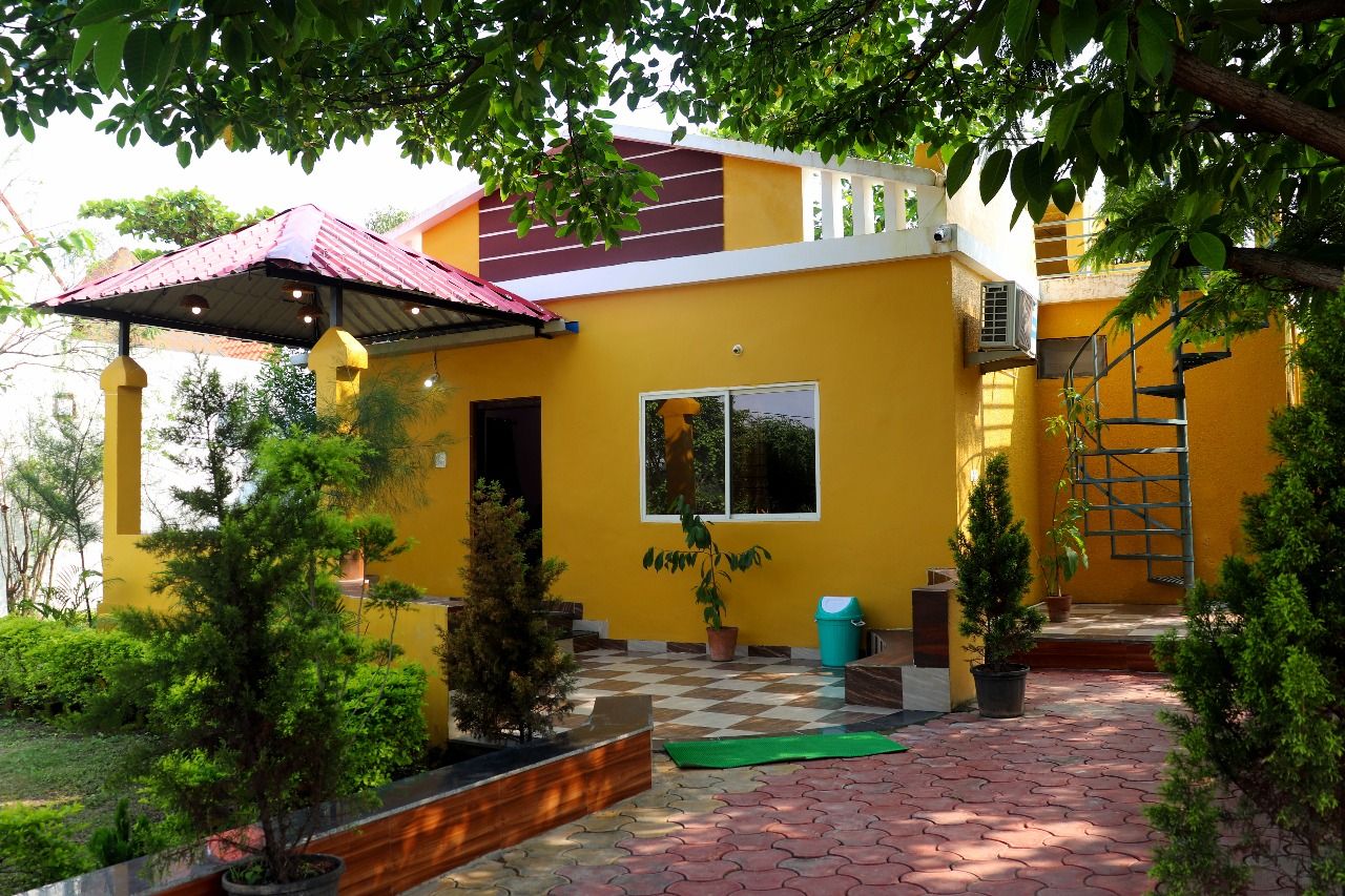 A yellow building with a red roof, a covered patio area, and potted plants.