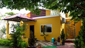 Un edificio amarillo con techo rojo, un patio cubierto y macetas con plantas.