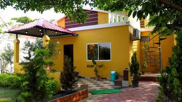 A yellow building with a red roof, a covered patio area, and potted plants.
