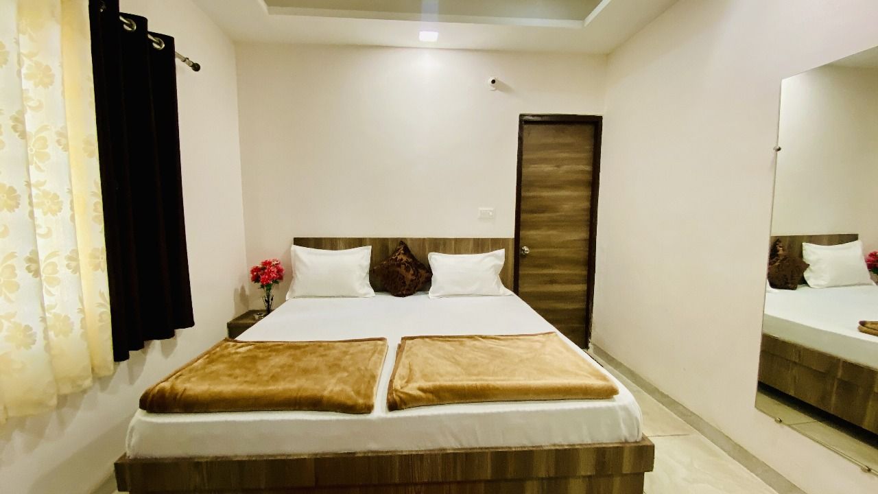 A hotel room with a bed, a mirror, a door, and a curtain.