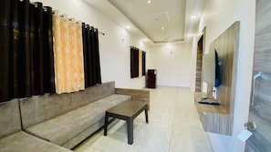 A living room with a sofa, a coffee table, and a flat-screen TV mounted on a wooden wall. - Mandu Green Villa  (Mandav)