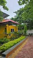 Un edificio amarillo con techo rojo, rodeado de vegetación y un sendero pavimentado.