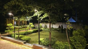 Zona exterior ben il·luminada amb un camí pavimentat, arbustos ben podats i un grup de persones reunides prop d'una paret.
