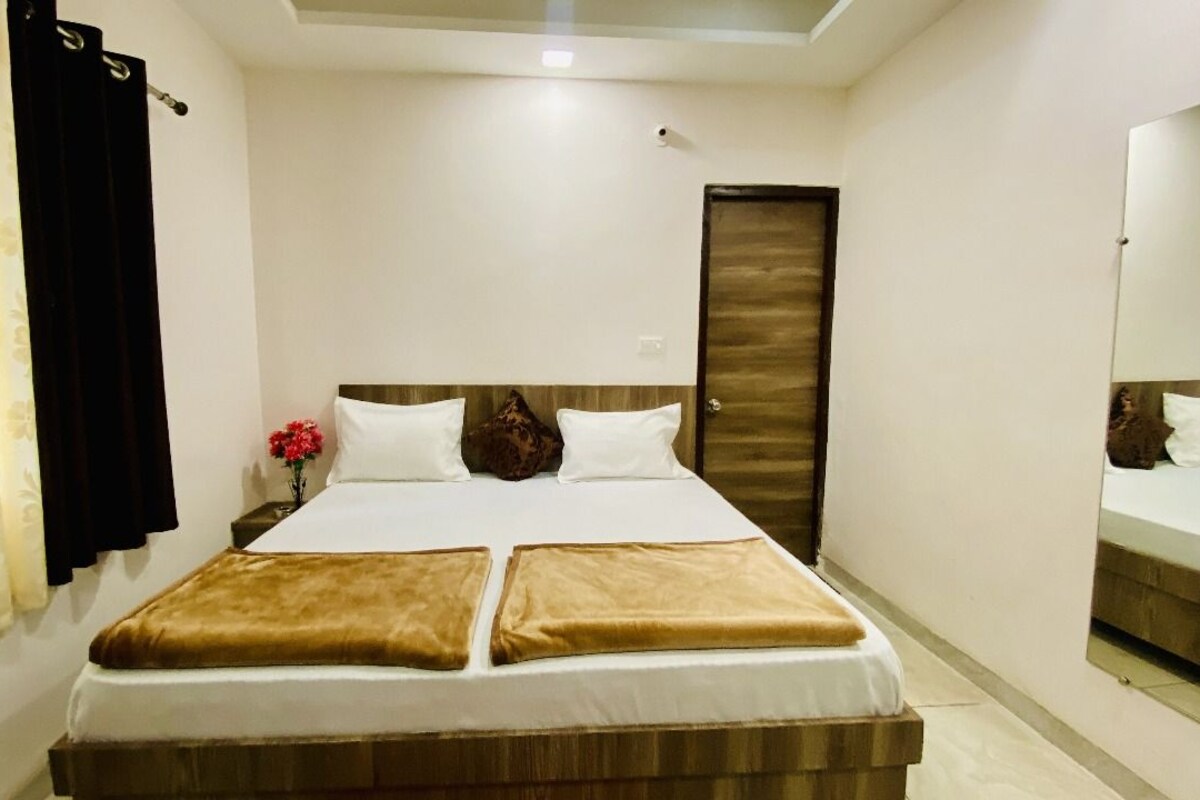 A hotel room with a bed, a mirror, a door, and a curtain.