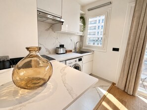 Ett modernt kök med en bänkskiva i marmor, en brödrost i rostfritt stål, en tvättmaskin och en stor vas.