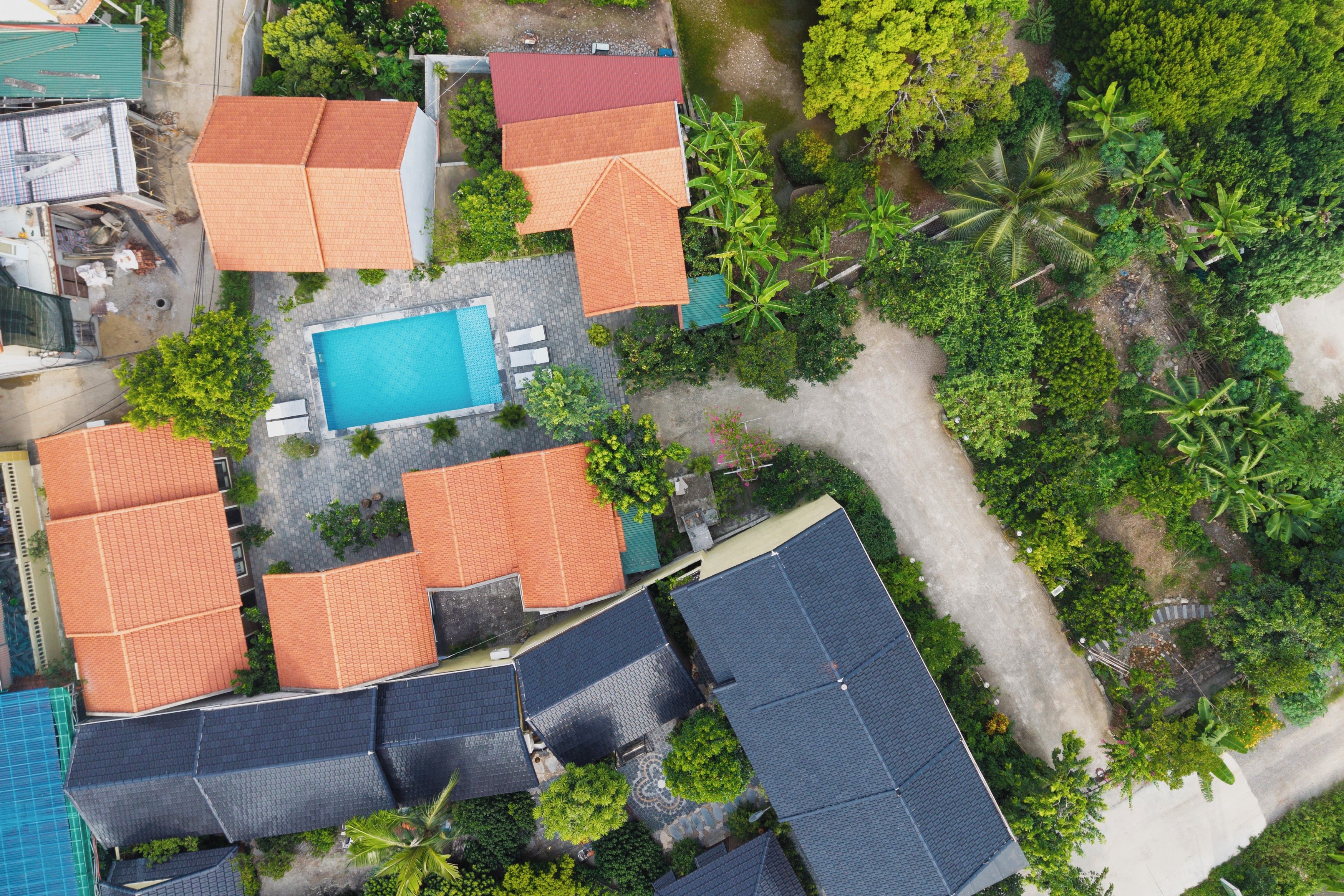 An aerial view of a residential area with multiple houses, a swimming pool, and surrounding greenery.