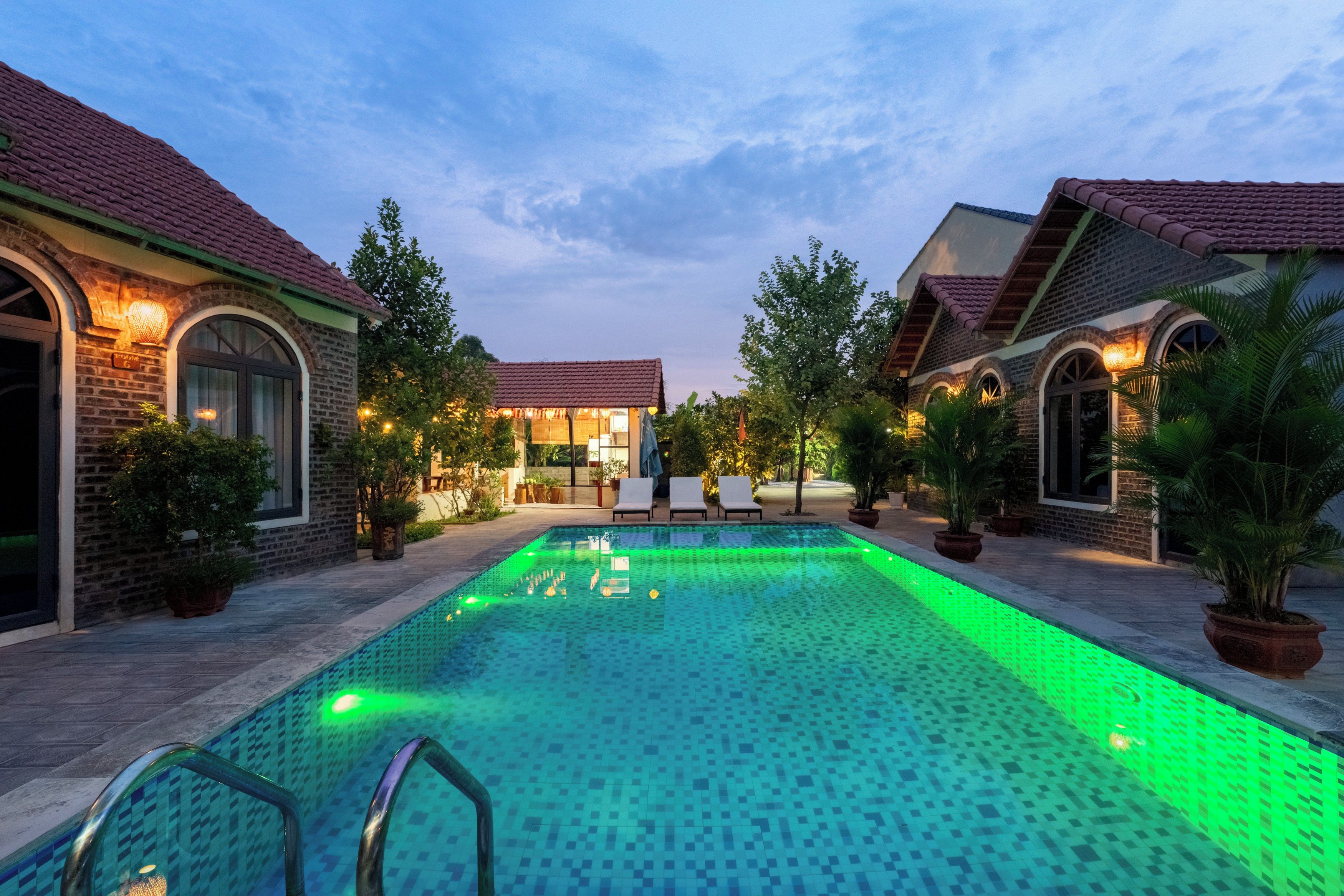 A swimming pool with a tiled pattern, surrounded by brick buildings with arched windows and doors, and potted plants.
