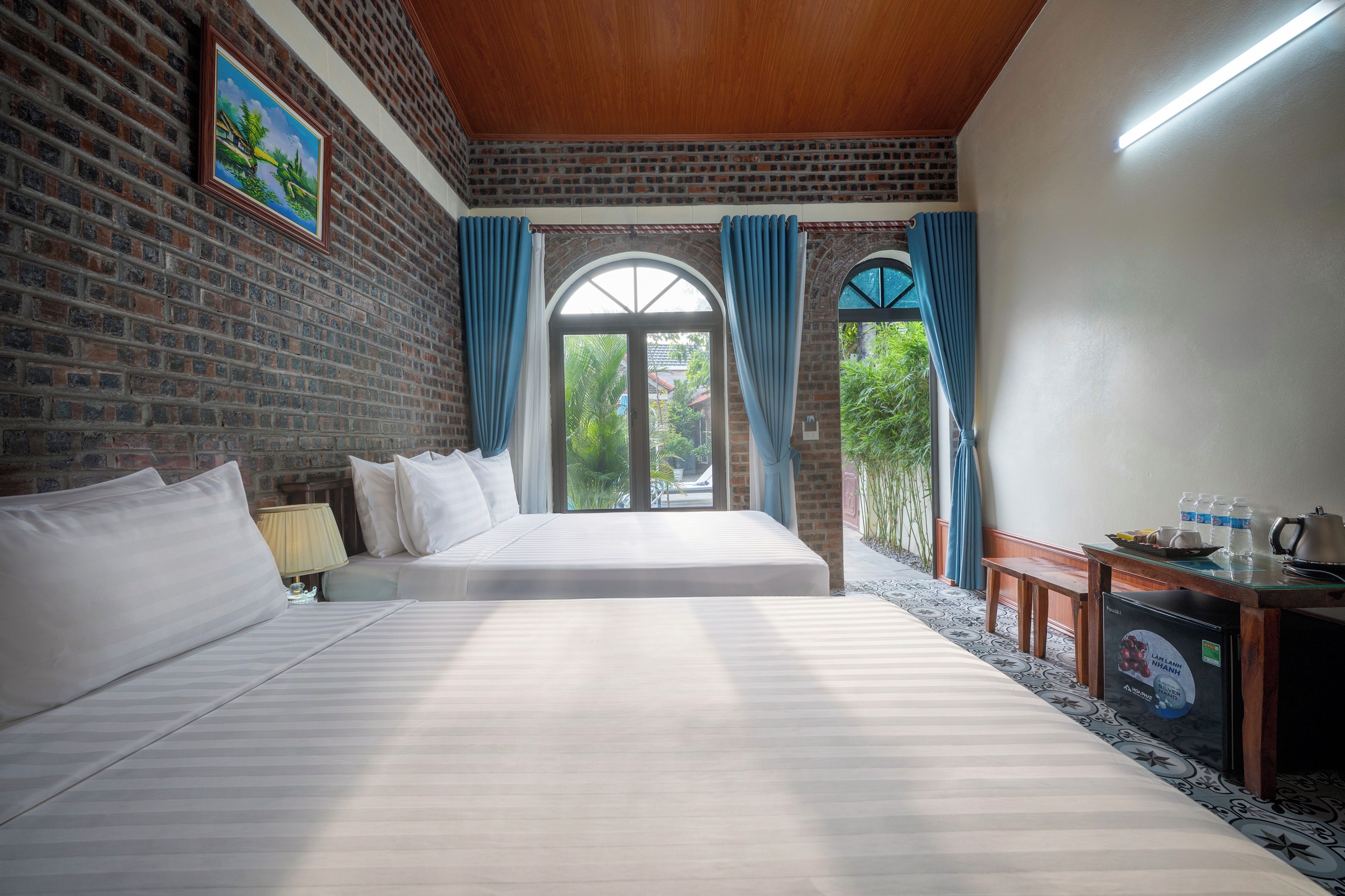 A hotel room with a large bed, a desk, and a view of greenery outside.