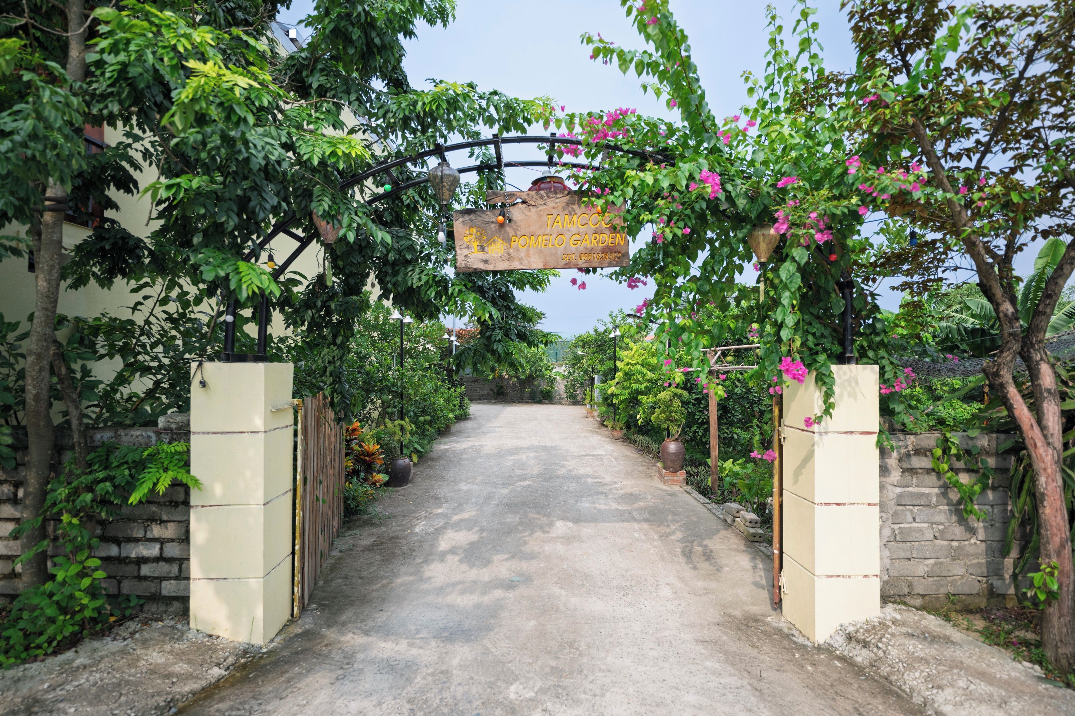 A gated entrance to a garden with a wooden sign, a concrete path, and lush greenery.