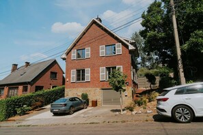 A two-story brick house with a garage, a car parked in front, and a tree in the driveway.