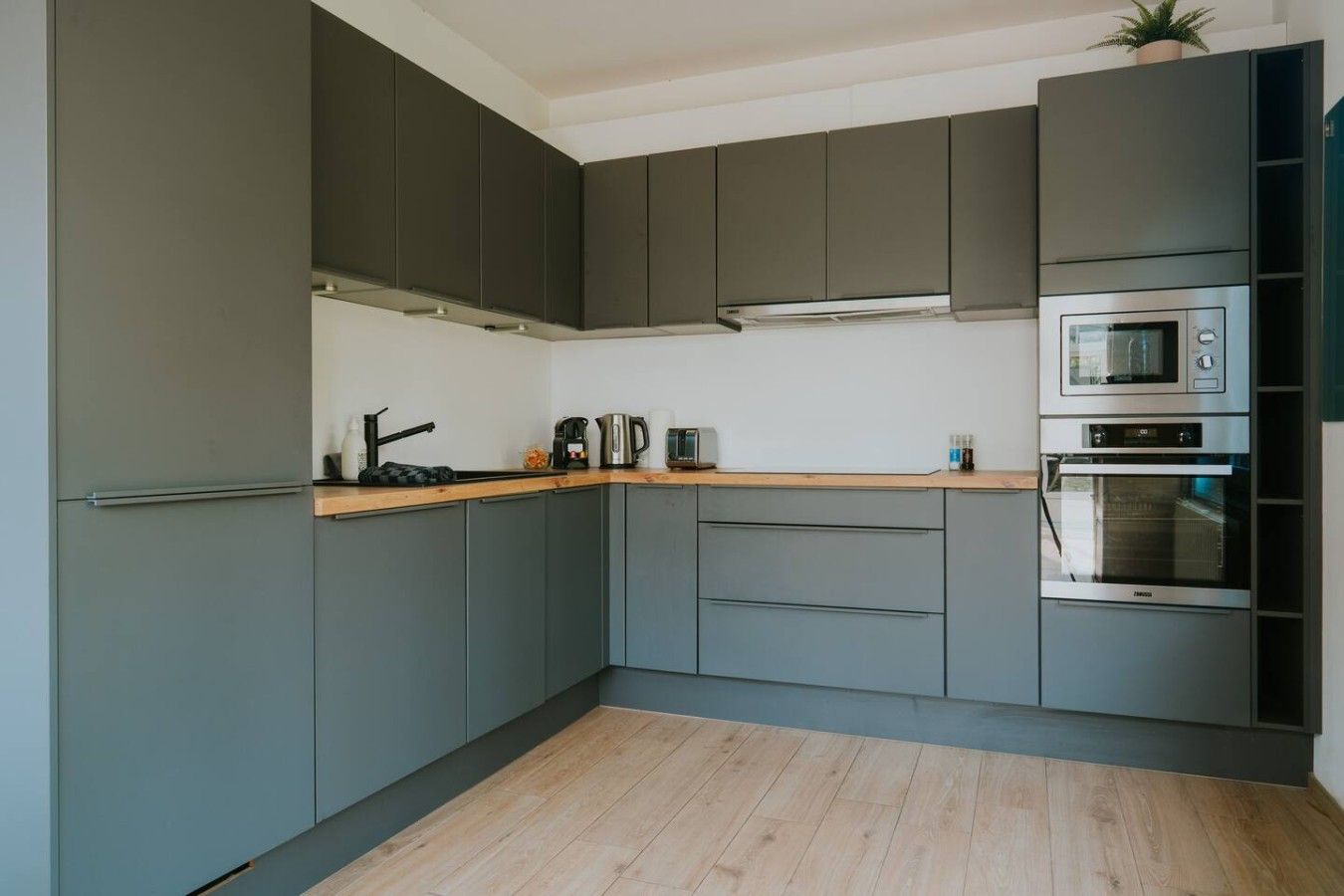 Eine moderne Küche mit grauen Schränken, einer Holz Arbeitsplatte und Edelstahlgeräten, darunter eine Mikrowelle und ein Backofen.