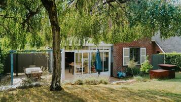 A house with a glass-enclosed patio, a brick exterior, and a tree in the foreground.
