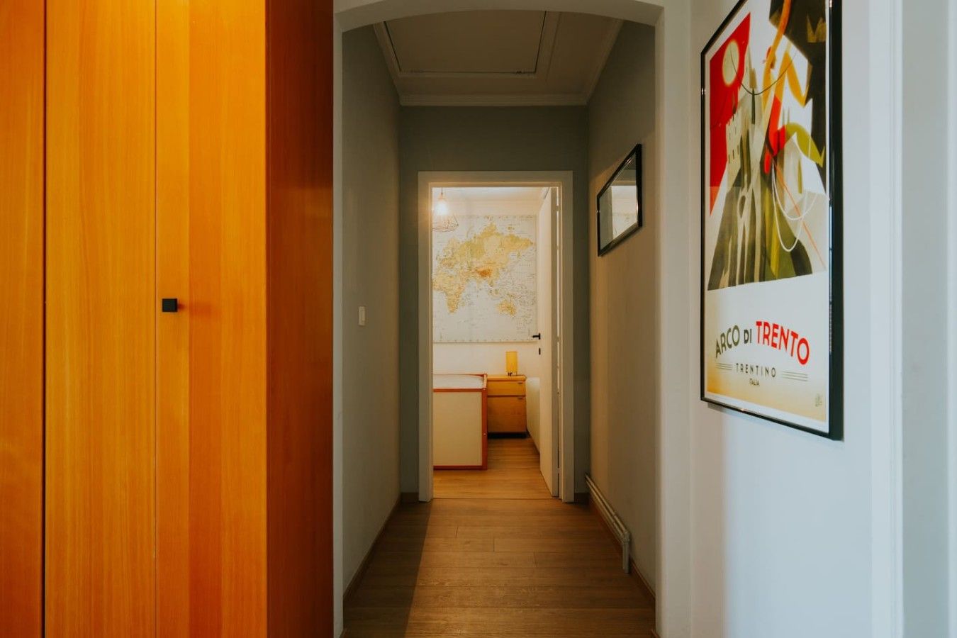 A hallway with a wooden door, a map on the wall, and a framed picture.