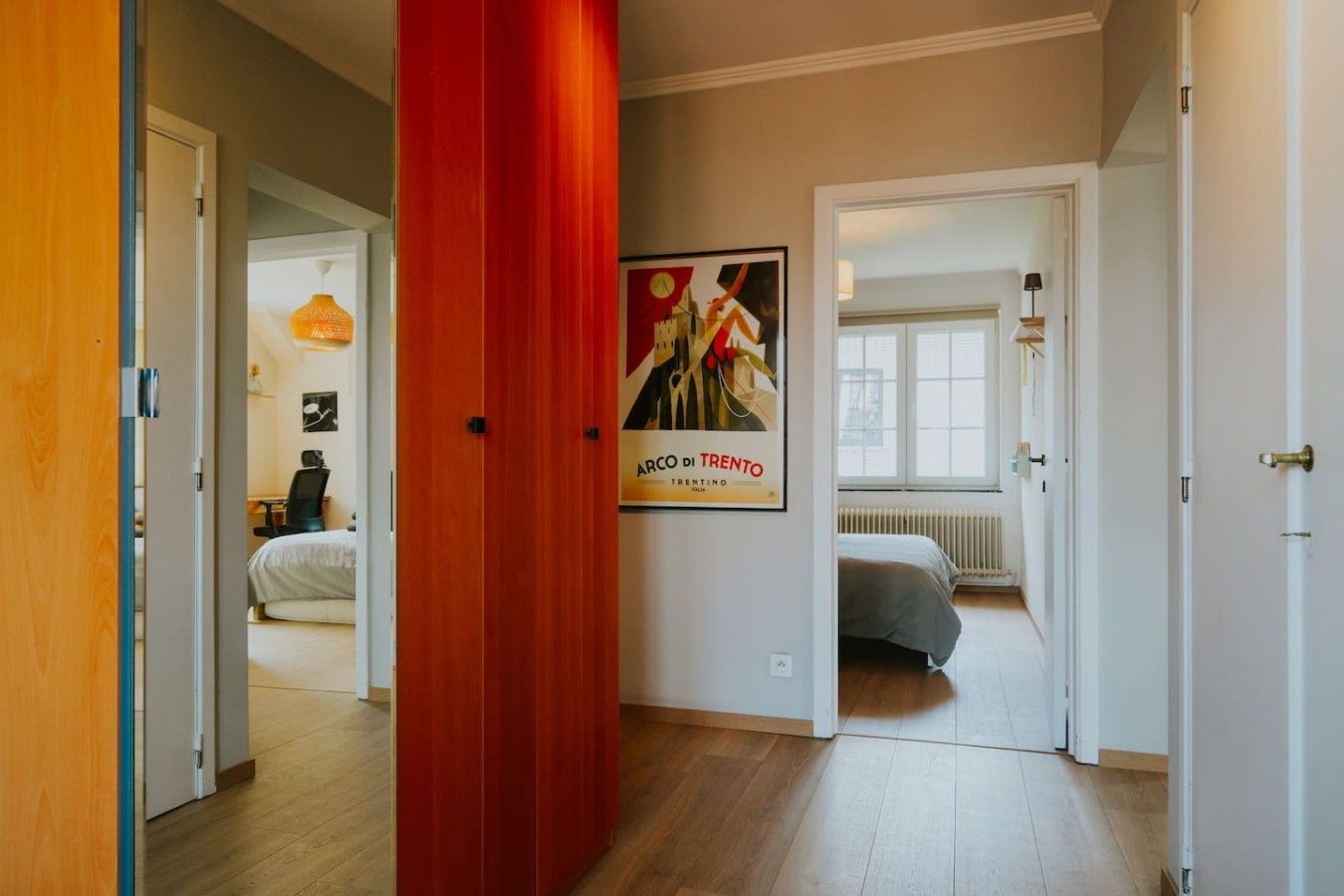 Hotelkamer met een bed, een bureau en een stoel. Een poster hangt aan de muur en er is een raam met uitzicht op buiten.