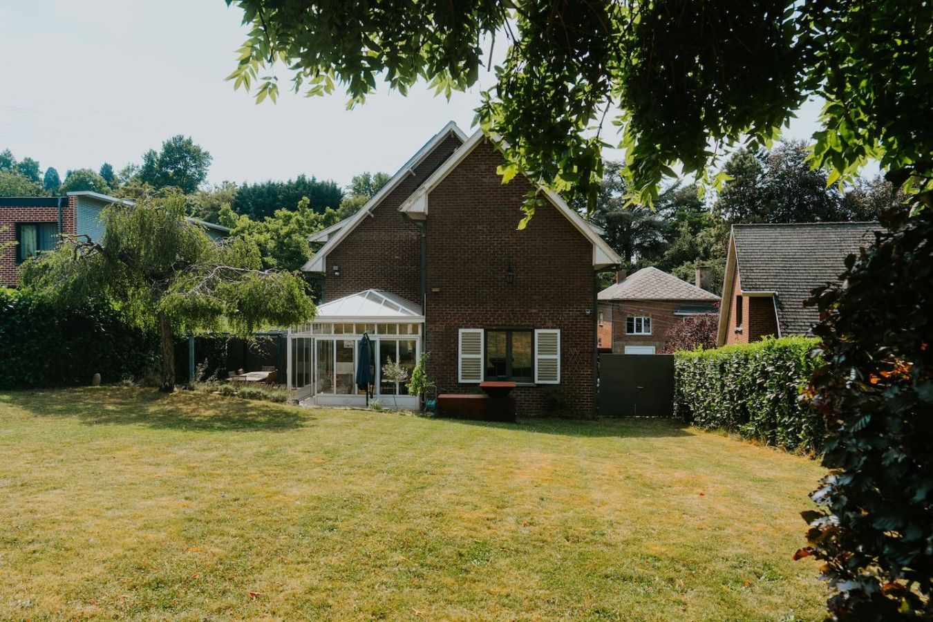 A residential property with a brick house, a conservatory, and a well-maintained lawn.