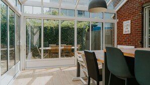Uma área de refeições moderna com um compartimento de vidro, parede de tijolos e vista para um jardim.