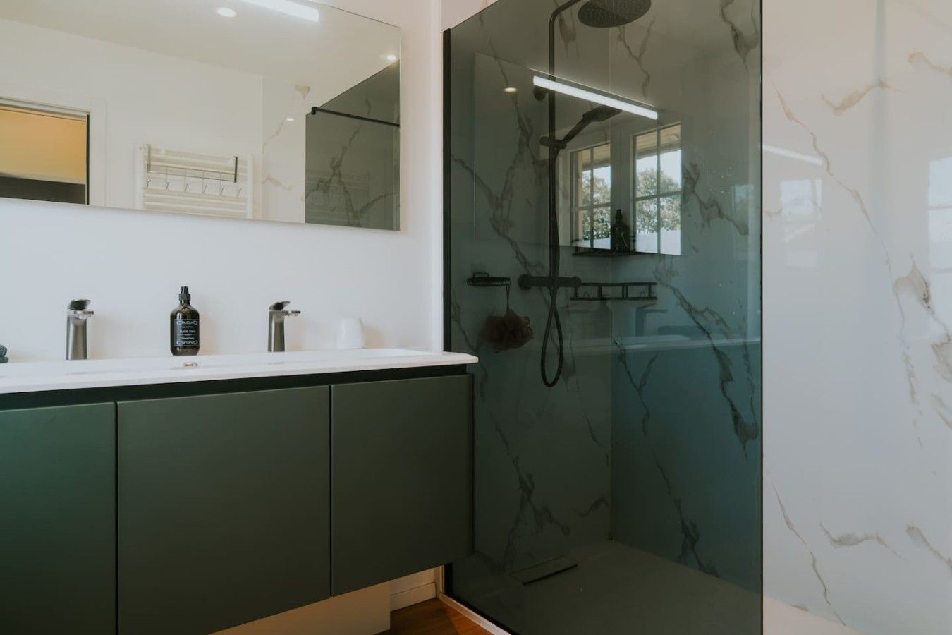 Een moderne badkamer met een douche met glazen wand, een grote spiegel en een donkerd washok.