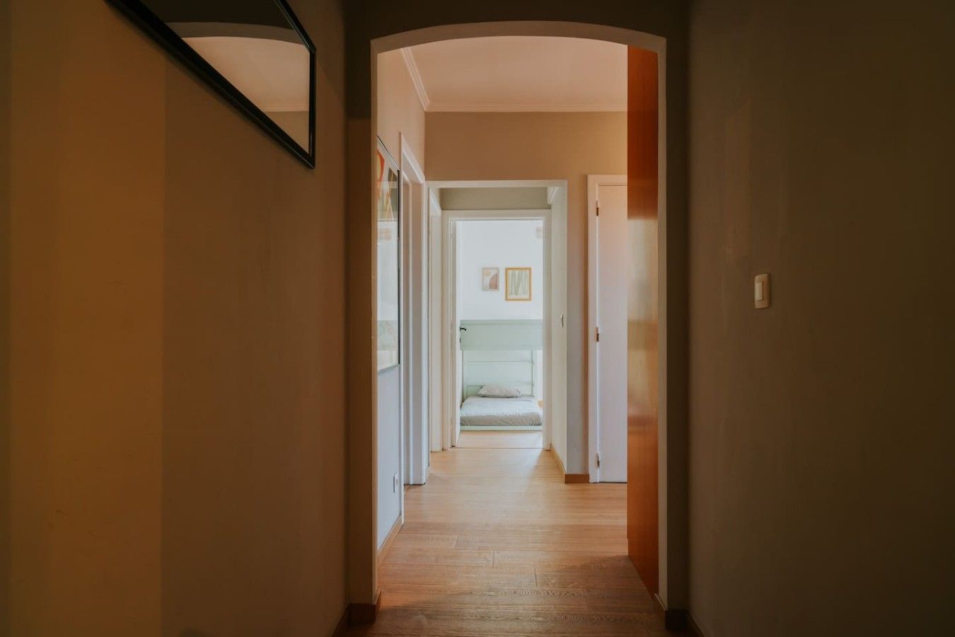 Een gang die leidt naar een slaapkamer met een bed, een deur en een lichtschakelaar op de muur.