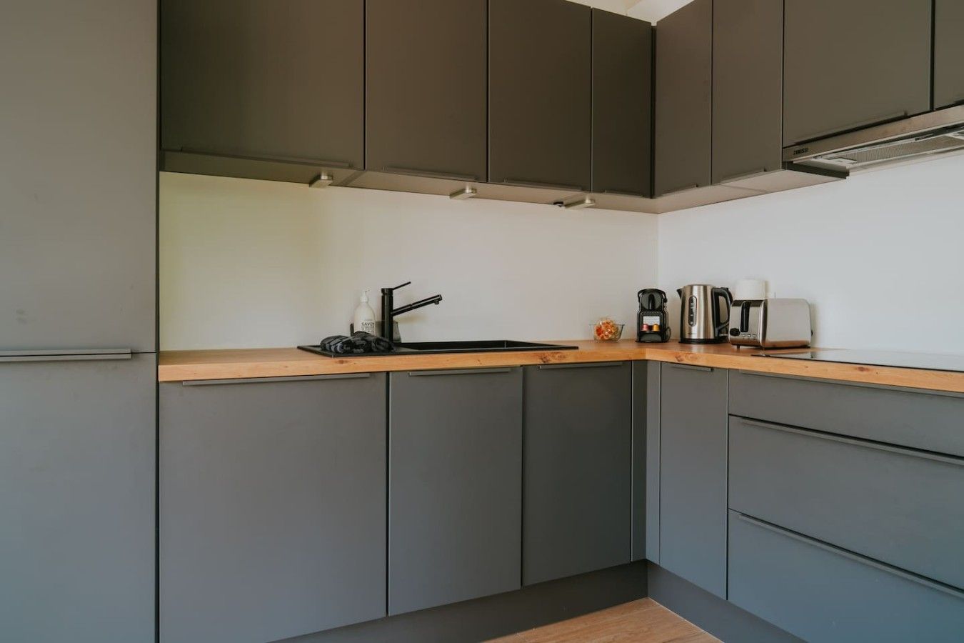 Une cuisine moderne avec des meubles gris, un plan de travail en bois et une machine à café.
