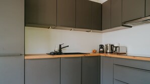Cozinha moderna com armários cinzas, bancada de madeira e cafeteira.