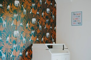 Ein Zimmer mit raumhoher Tapete mit Muster, einem weißen Schrank und einer an der Wand befestigten Buchstabenleiste.