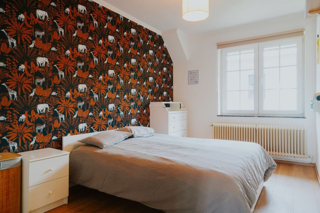 Una camera da letto con un letto, una cassettiera, un termosifone e una finestra.