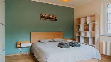 Un dormitorio con cama, mesita de noche, estantería y una obra de arte en la pared.