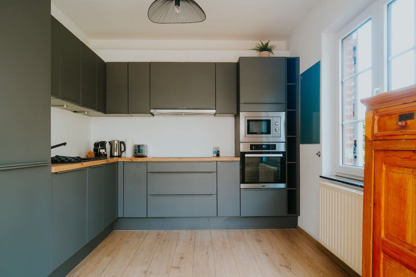 Een moderne keuken met grijze kastjes, een houten aanrechtblad en inbouwapparatuur, waaronder een magnetron en oven.