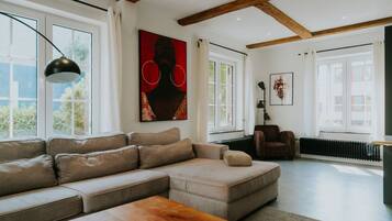Ein modernes Wohnzimmer mit einem Ecksofa, einem Couchtisch aus Holz und Kunstwerken an den Wänden.