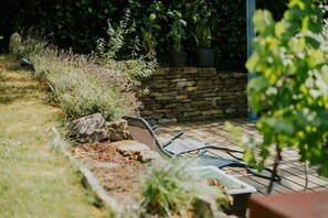 Ein Garten mit einer Steinmauer, einem Metallstuhl und einem Gartenschlauch.