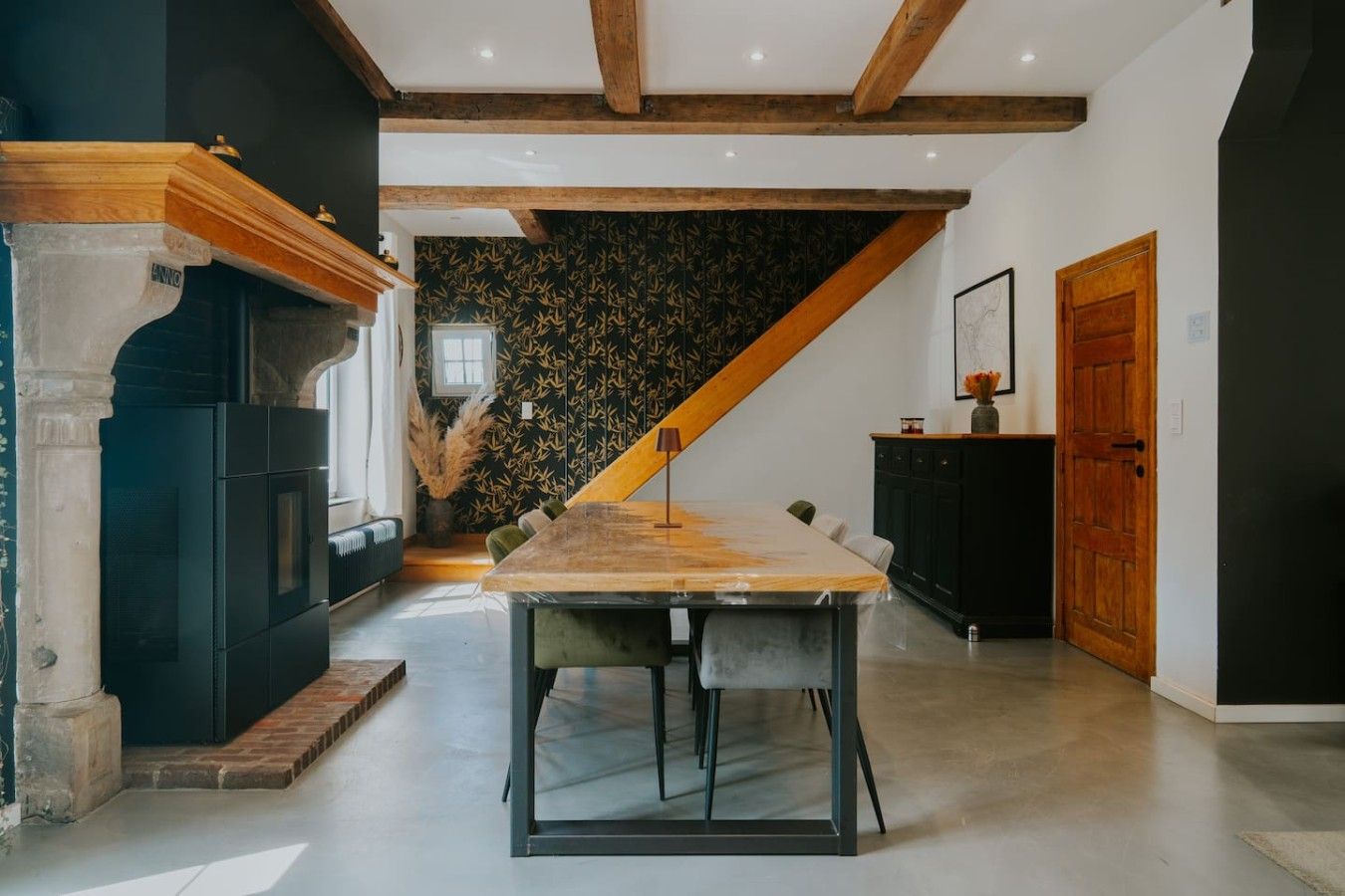 Une cuisine moderne avec une table à manger en bois, des meubles de rangement noirs et un escalier menant à un niveau supérieur.