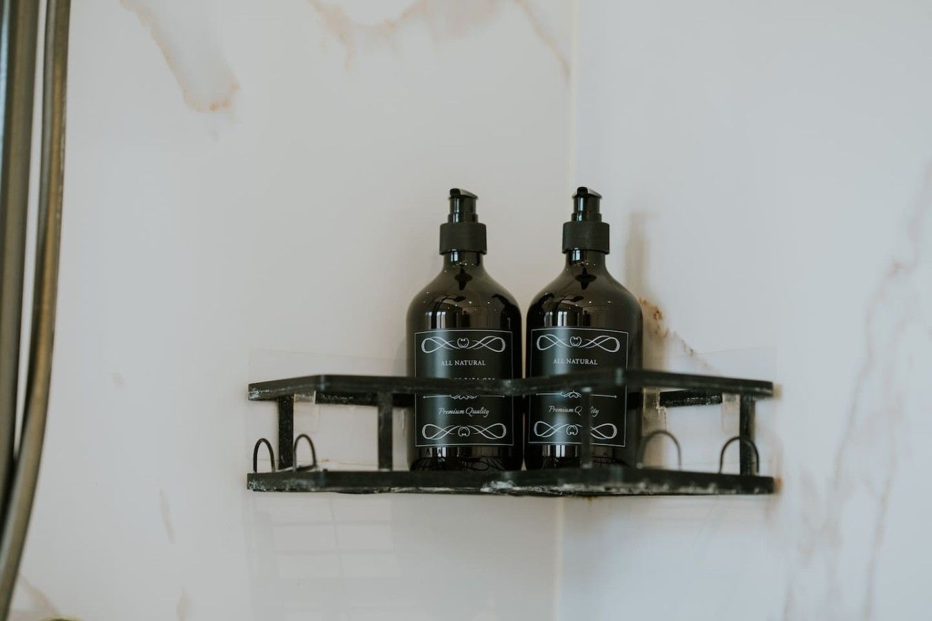 Deux bouteilles de gel douche de qualité supérieure, entièrement naturel, sont posées sur une étagère en métal noir, devant un mur blanc.