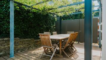 A wooden deck with a table and chairs, surrounded by a stone wall and greenery.