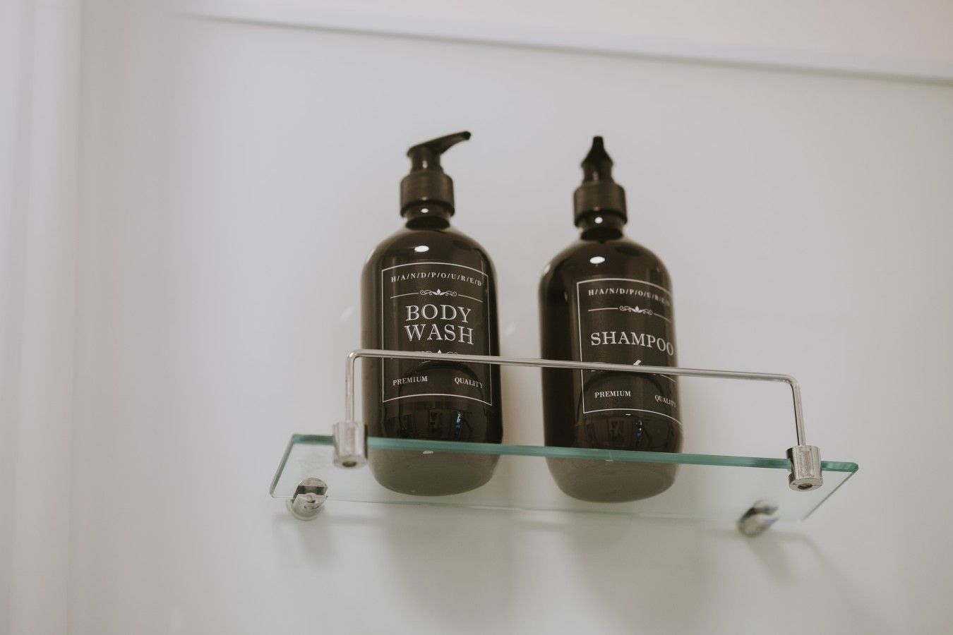 Deux bouteilles de gel douche et de shampoing sont posées sur une étagère en verre transparent.