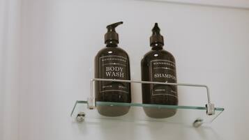 Deux bouteilles de gel douche et de shampoing sont posées sur une étagère en verre transparent.