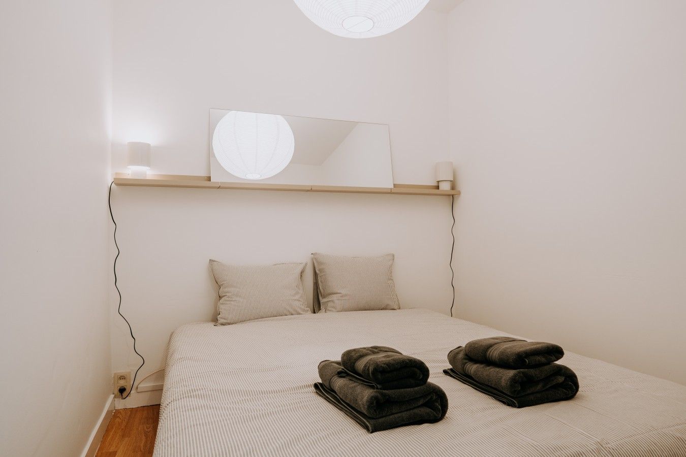 Ein Schlafzimmer mit einem Bett, zwei Kissen, einem Spiegel und zwei gerollten Handtüchern auf dem Bett.