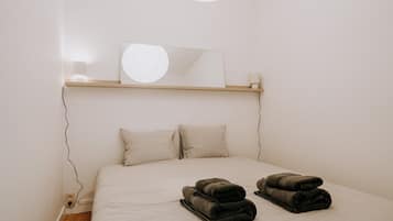 Ein Schlafzimmer mit einem Bett, zwei Kissen, einem Spiegel und zwei gerollten Handtüchern auf dem Bett.